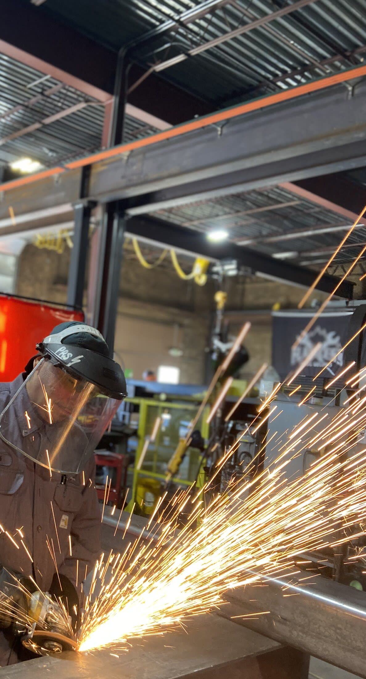 Welder working with sparks inside the Flawless Steel Welding fabrication shop.
