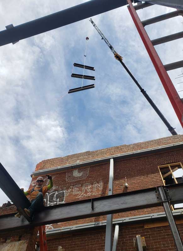 A low angle shot of a crane lifting three steel beams.