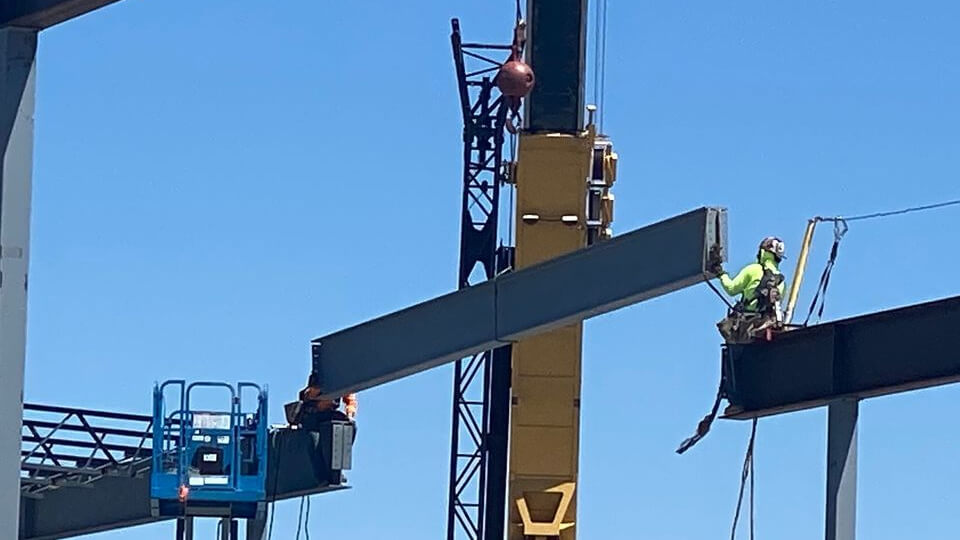 Construction workers lift a steel beam using a crane.