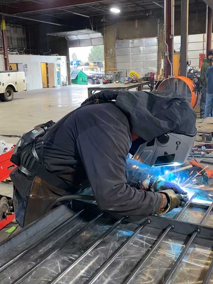 A well-trained welder inside a steel fabricating facility is working on steel.