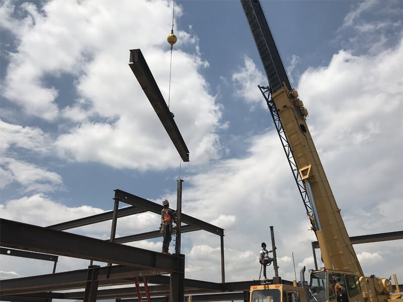 Ground shot of a crane truck lifting a steel beam.
